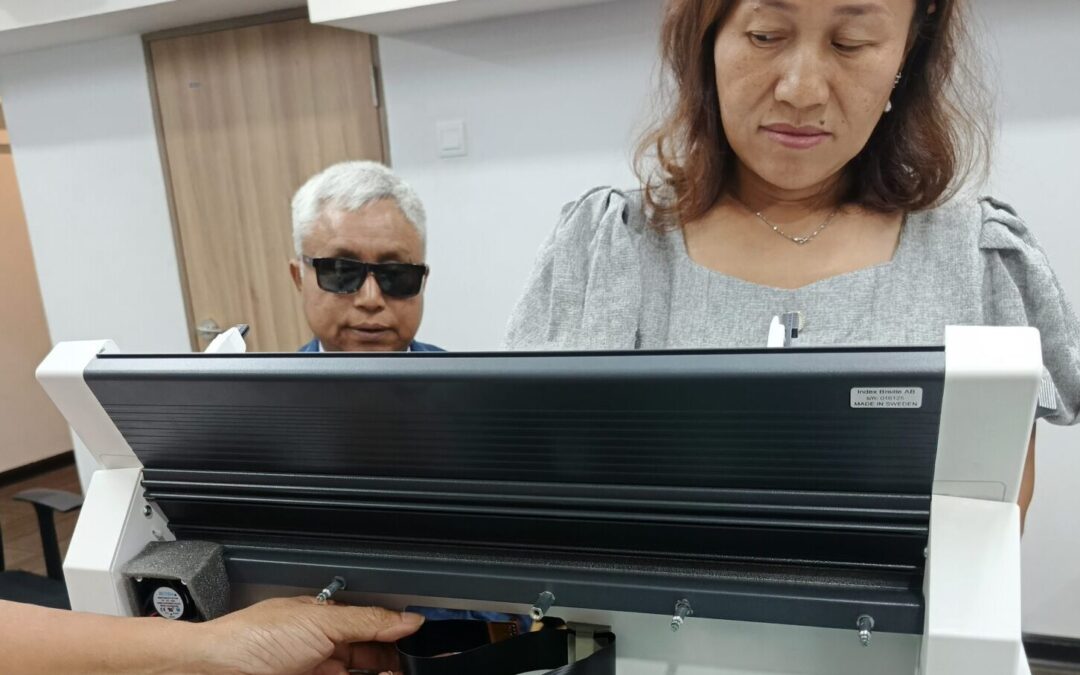 Mrs. Kwai Nan, Mitarbeiterin der HBM in Myanmar, mit dem Schulleiter U Tin Moe vor dem neuen Brailledrucker
