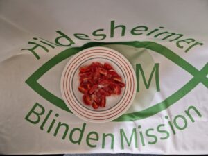 Eine Schüssel mit geviertelten Tomaten mit Zucker bestreut. Als Untergrund eine Tischdecke mit dem Logo der HBM.