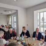 viele Menschen sitzen an Tischen und löffeln chinesische Suppe und Essen Brot dazu, die Tische sind mit einzelnen Tulpen, Butterstücke auf kleinen Tellern, Brotkörbchen, Getränken in Flaschen und Karaffen, Gläsern, Teelichtern und in der Mitte jeden Tisches ein Ulos geschmückt. Im Hintergrund ist eine Fensterreihe