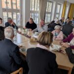 viele Menschen sitzen an Tischen und löffeln chinesische Suppe und Essen Brot dazu, die Tische sind mit einzelnen Tulpen, Butterstücke auf kleinen Tellern, Brotkörbchen, Getränken in Flaschen und Karaffen, Gläsern, Teelichtern und in der Mitte jeden Tisches ein Ulos geschmückt. Im Hintergrund ist die Fensterreihe, die zum Neustädter Markt schaut