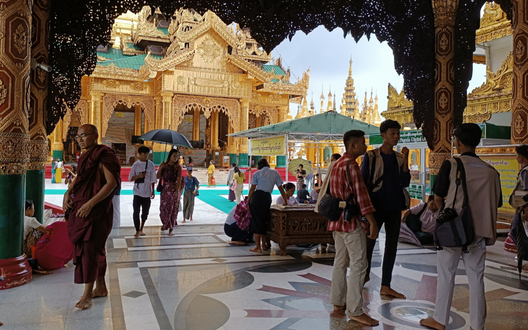 Rechts steht eine dreier Gruppe Männer in westlicher Kleidung mit Hemd, Westen und Hosen. Links im Bild ist ein Mönch in dunkelrotem Gewand mit Brille. Etwas weiter hinten im Bild läuft ein Pärchen, Frau und Mann, mit Sonnenschirm auf den Betrachter zu. Der Fußboden ist aus Marmor mit Muster und im Hintergrund sieht man vergoldete Säulen und Pagodenbögen und Giebel. Außerdem sind weitere Menschen im Bild.