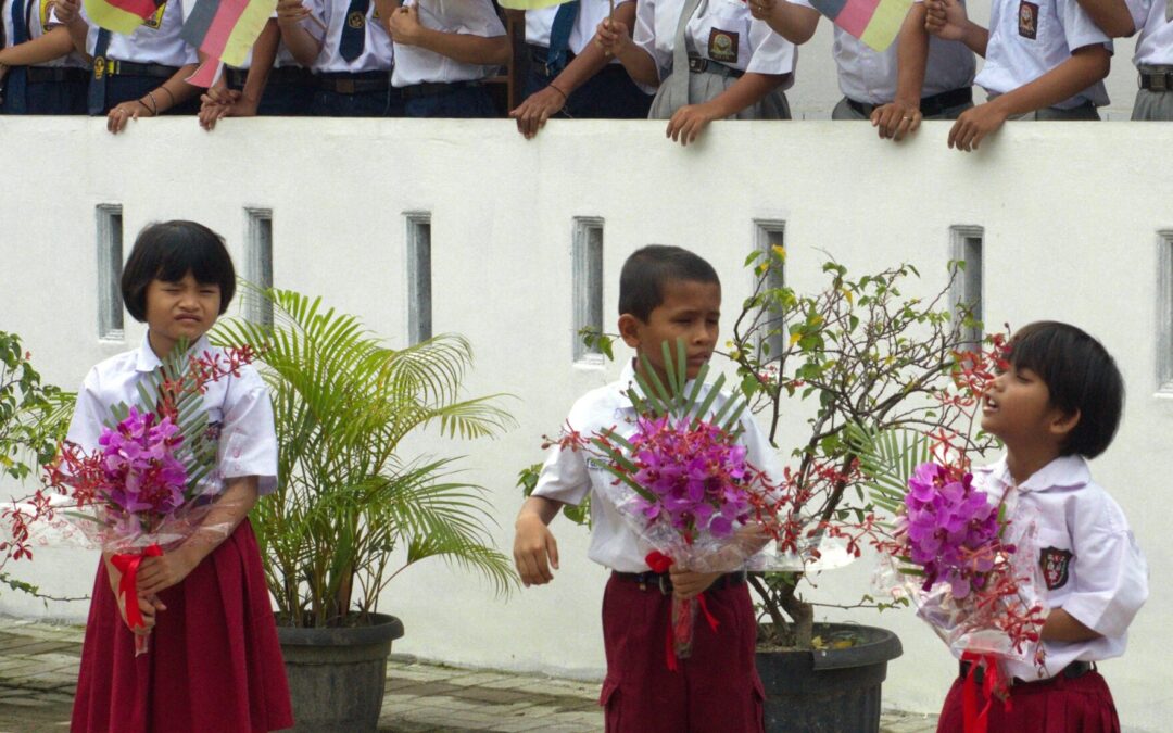 Kinder winken zur Begrüßung der HBM Delegation mit Deutschlandfähnchen und überreichen rosafarbene Blumen